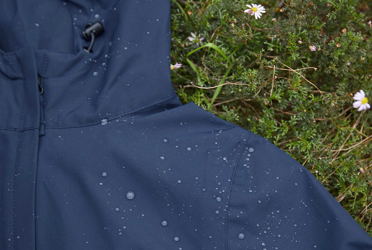 Amble elements jacket in black on the grass with water beading on the fabric